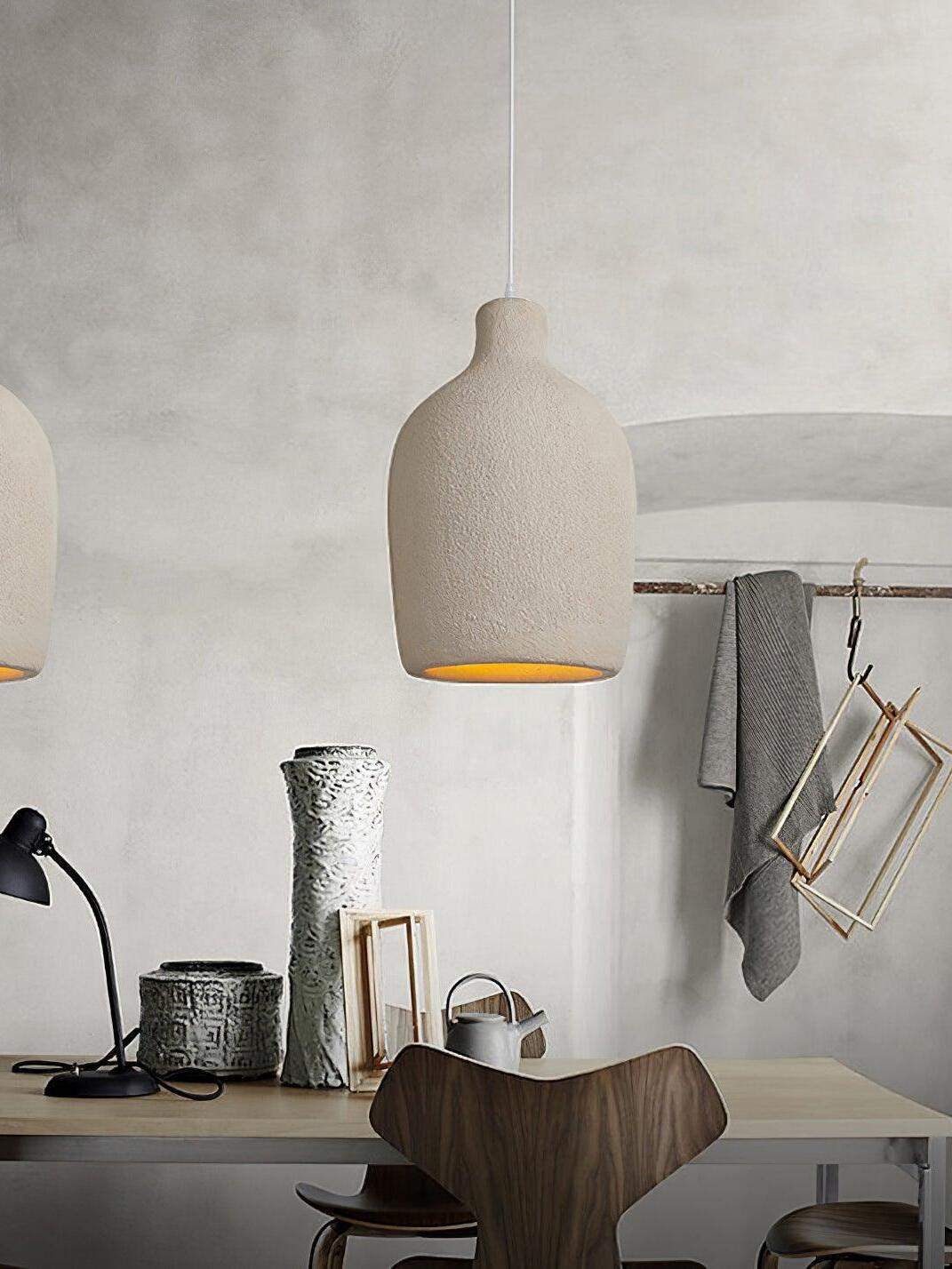 Bottle pendant above a wood worktable with dark chair, vessels, watering can, desk lamp and hanging frames
