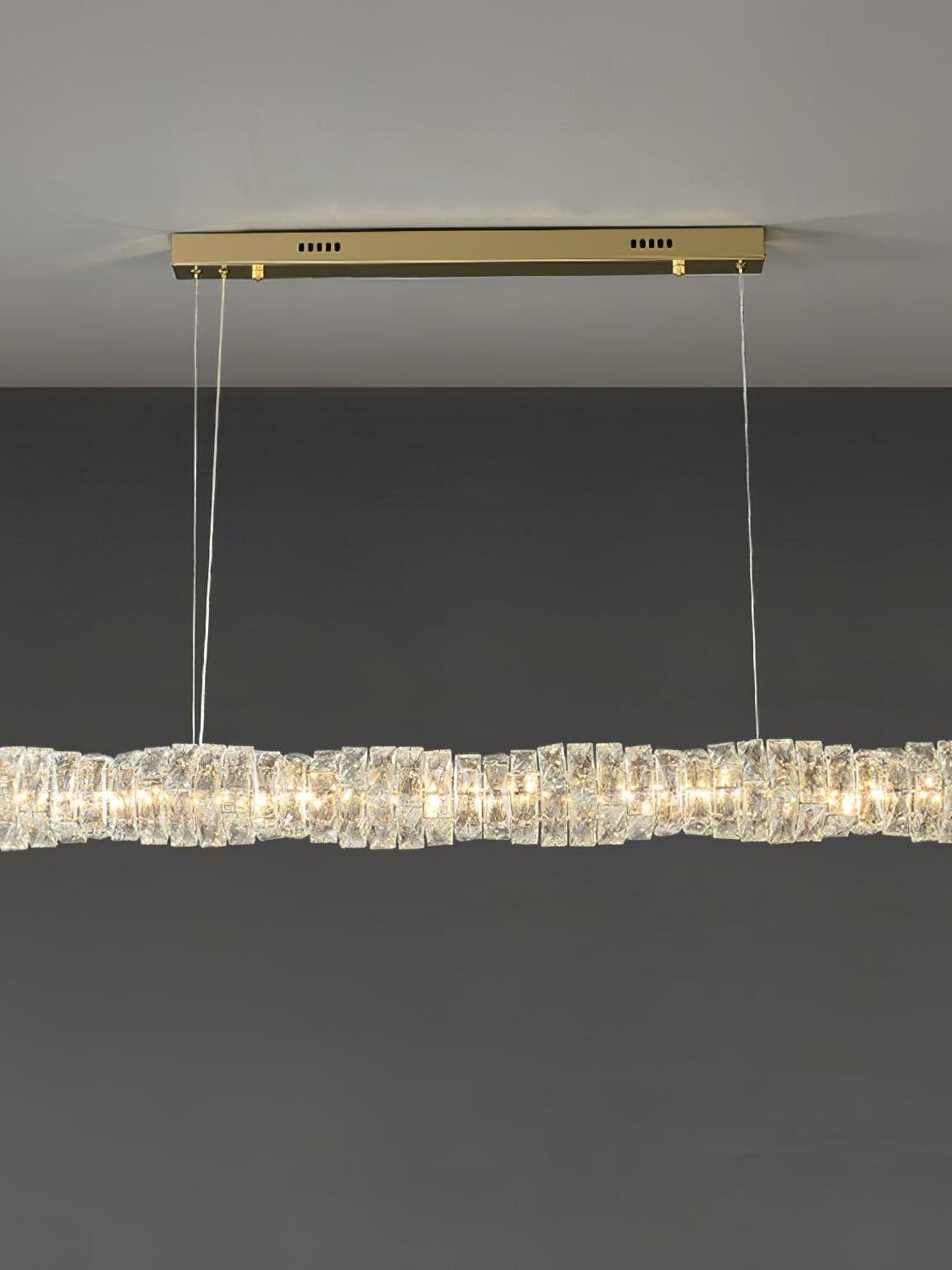 Front view of the gold canopy and long crystal bar emitting warm-looking light against a grey wall