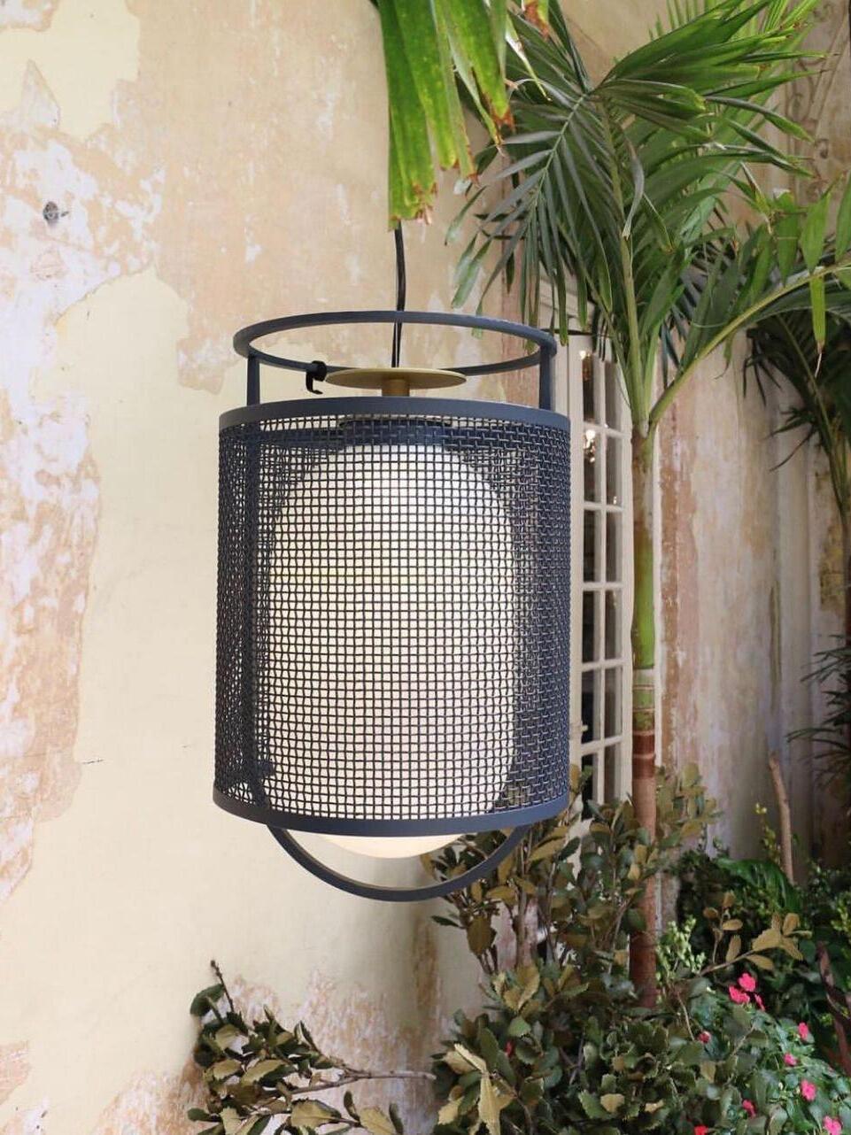 Black mesh pendant among plants beside weathered wall