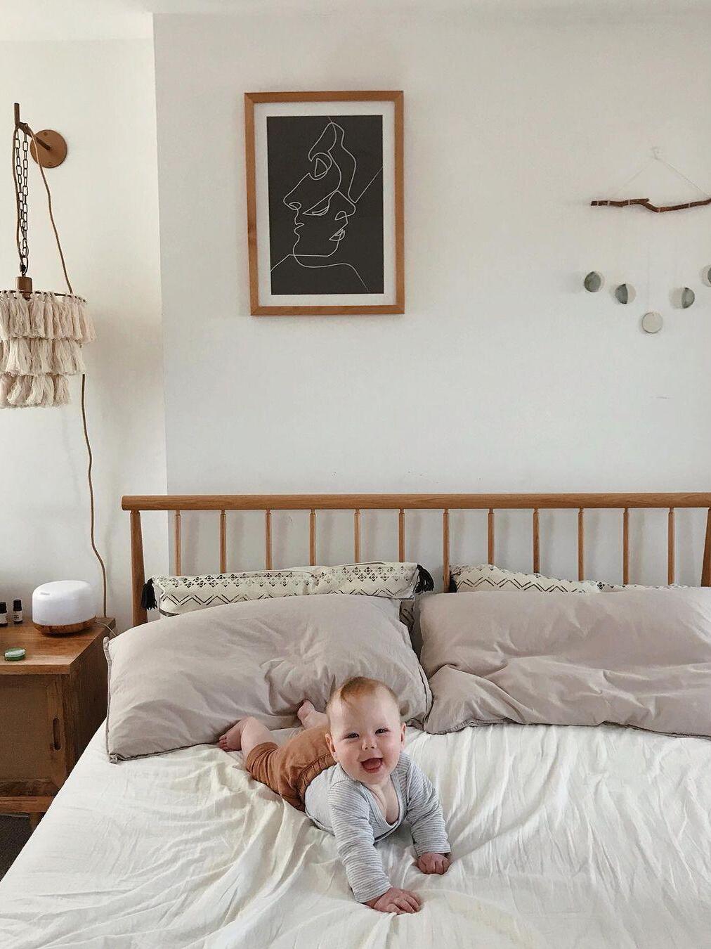White tassel wall light beside a wooden bed beneath framed artwork
