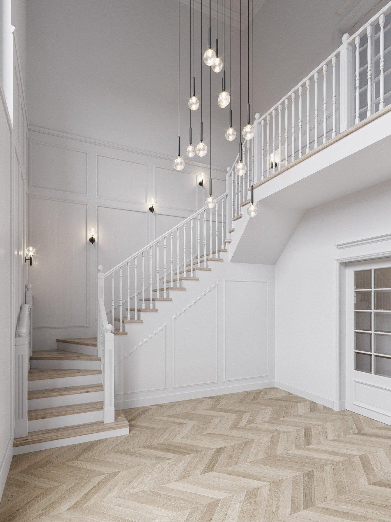 Staggered clear globe pendants with black stems above a tall white staircase and separate wall lights