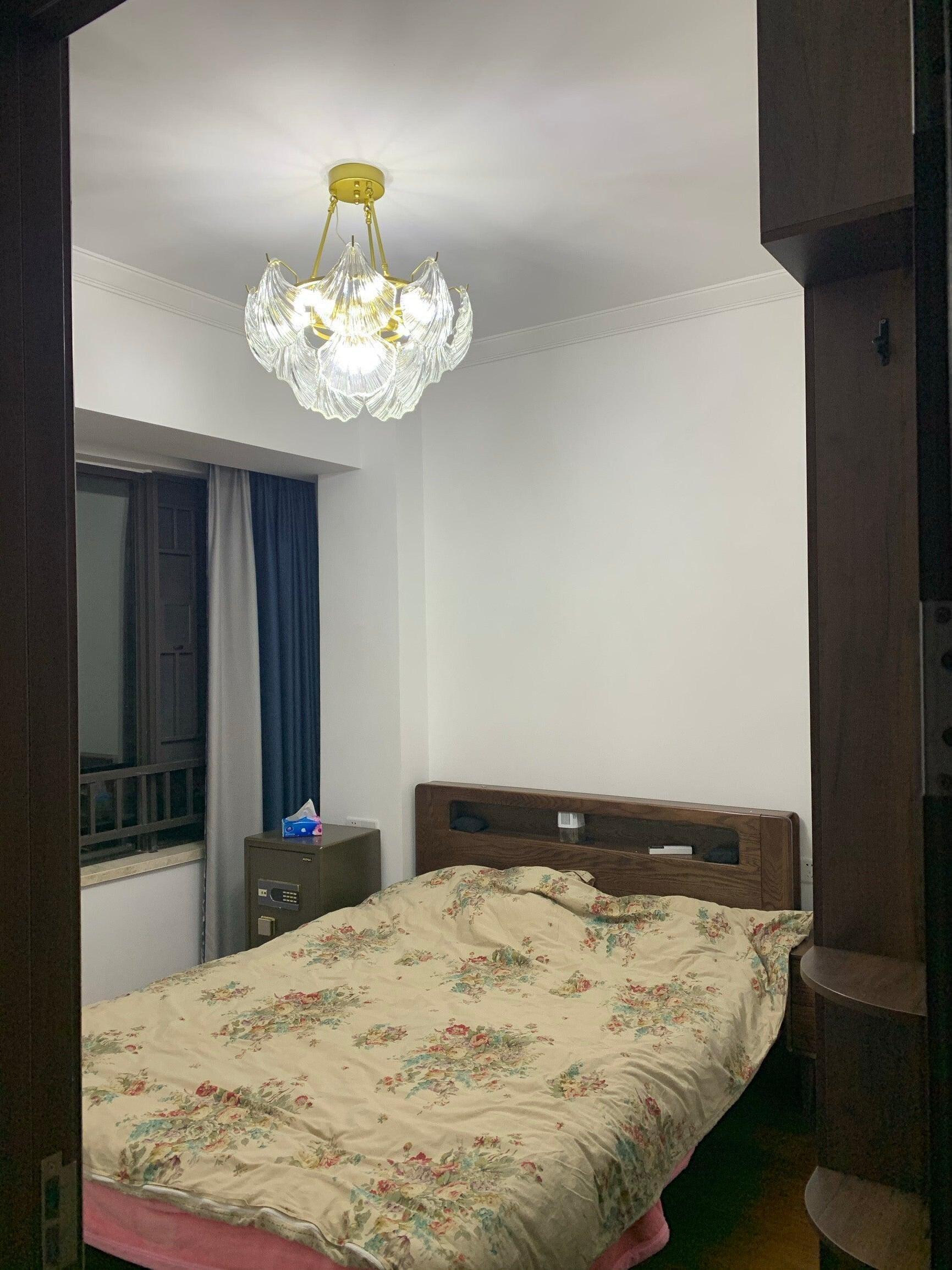 Round glass fixture above floral bedding beside a dark cabinet