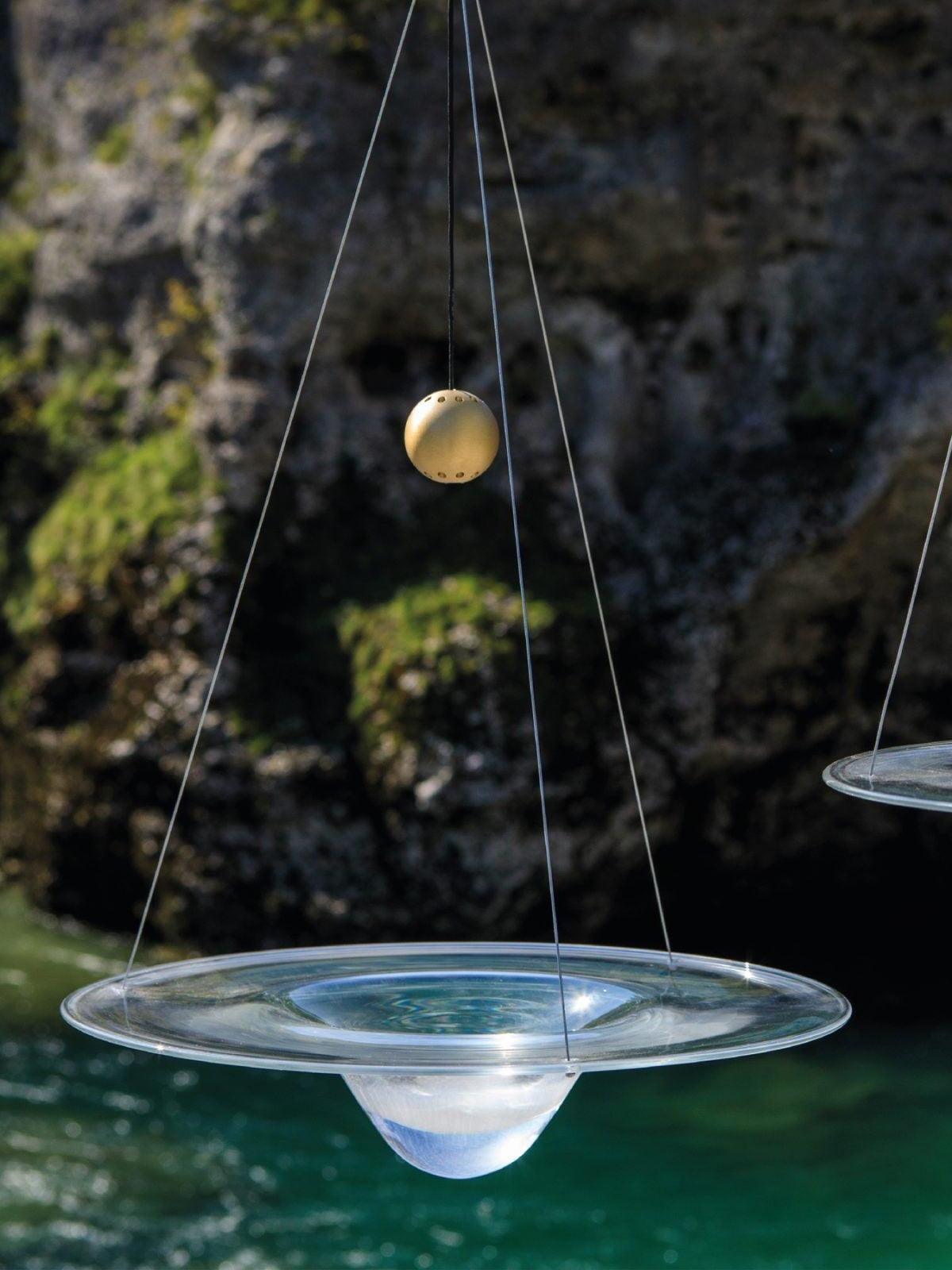 Brass ball above glass disc with rock and water behind