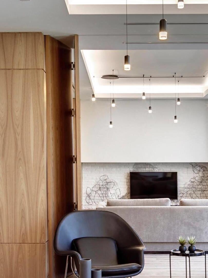 Lit ceiling pendants above a lounge armchair beside a wood partition and fireplace