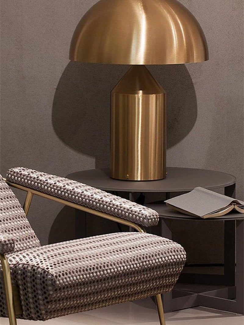 Gold-tone dome table lamp on a round side table with a book beside a patterned armchair