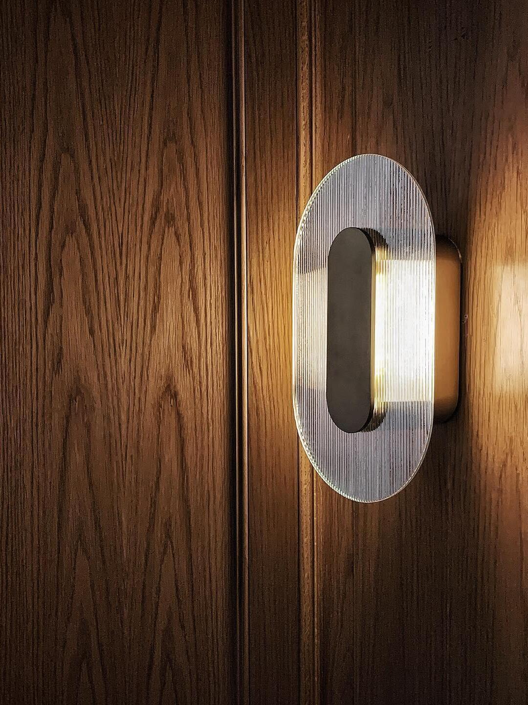 Lit elongated Button wall light on wood panelling, showing ribbed glass and the projecting rear housing