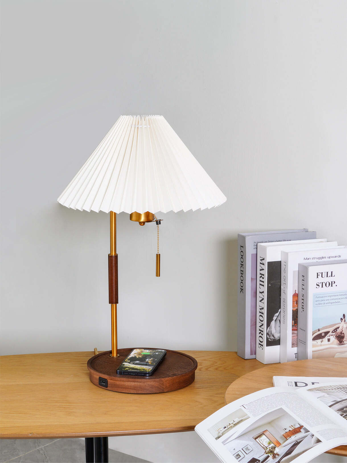 White pleated lamp with a phone on its round base and an open magazine on the desk