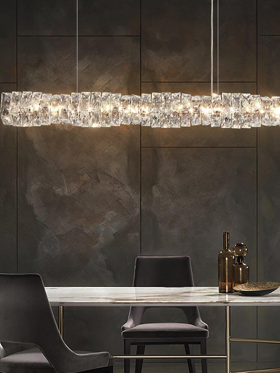 Front view of the long crystal pendant above a dining table against a dark stone wall