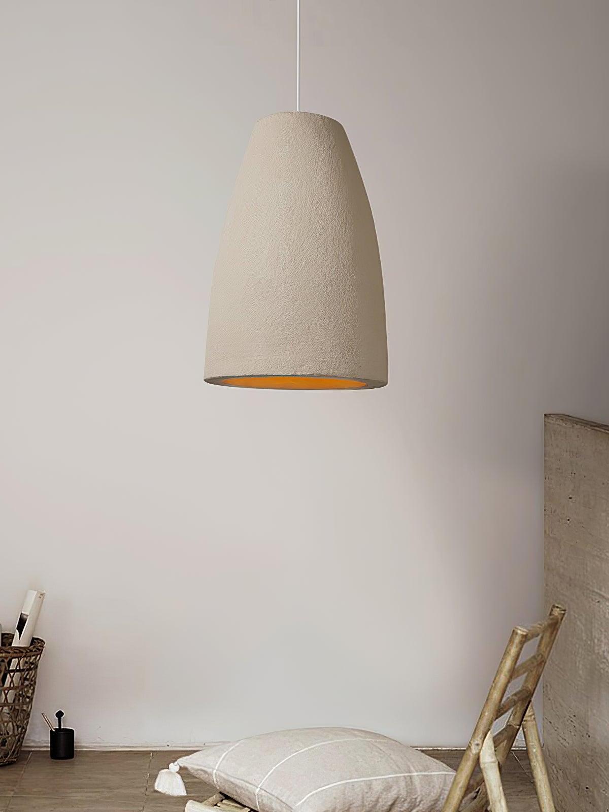 Wide tapered pendant beside a woven low chair, pale tasseled cushion, basket and leaning panel