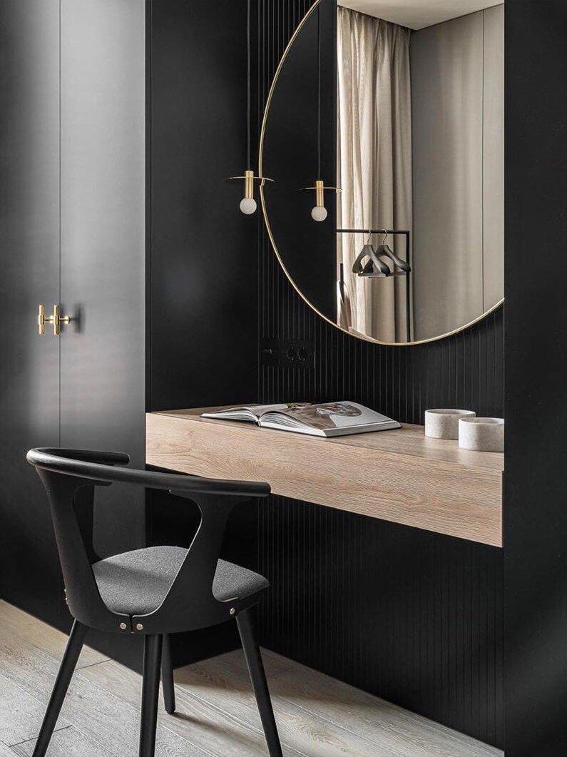 Brass-tone disc pendant and its reflection above a wooden console beside a round mirror