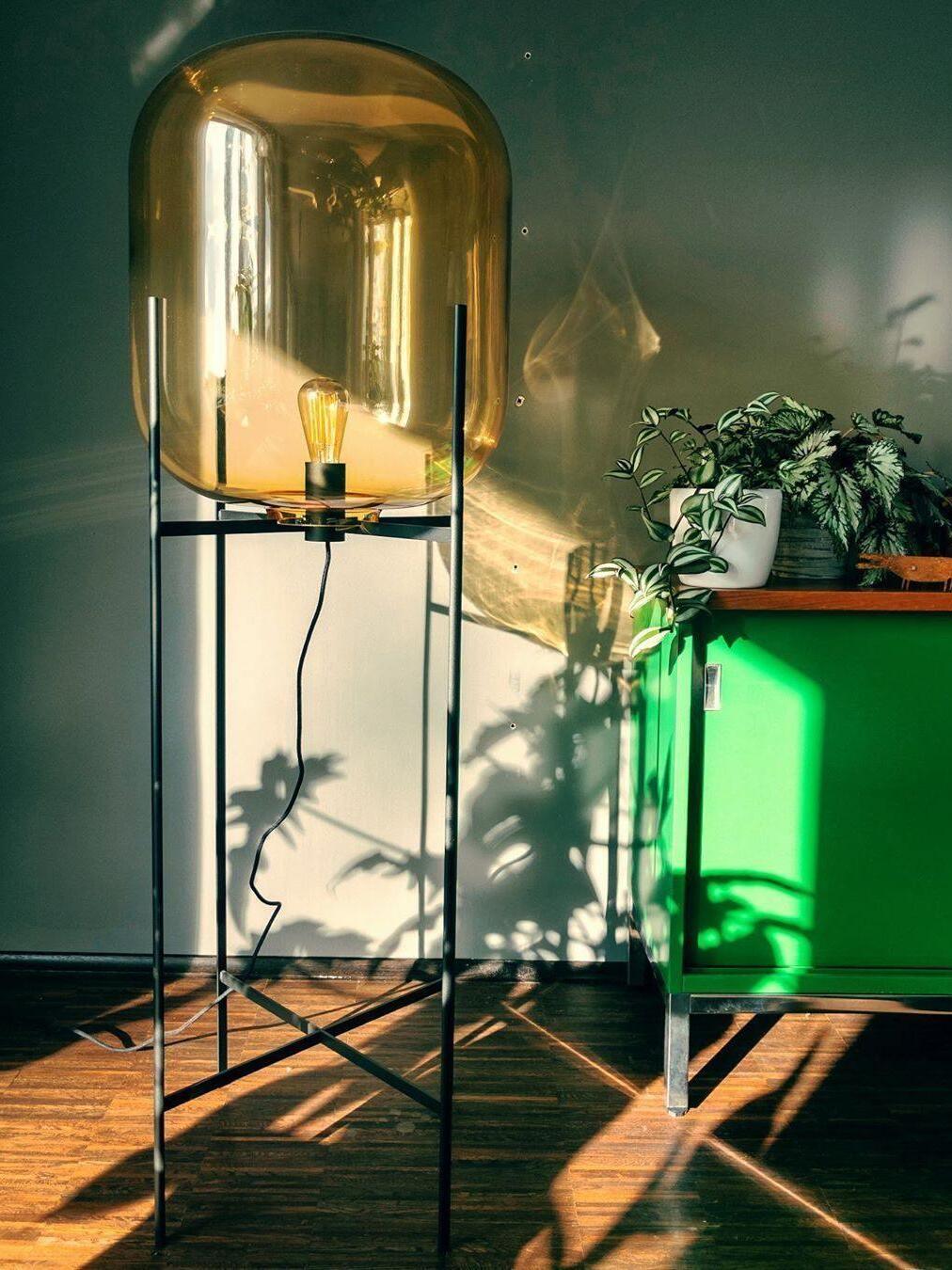 Amber glass shade and black open stand casting shadows near a plant.