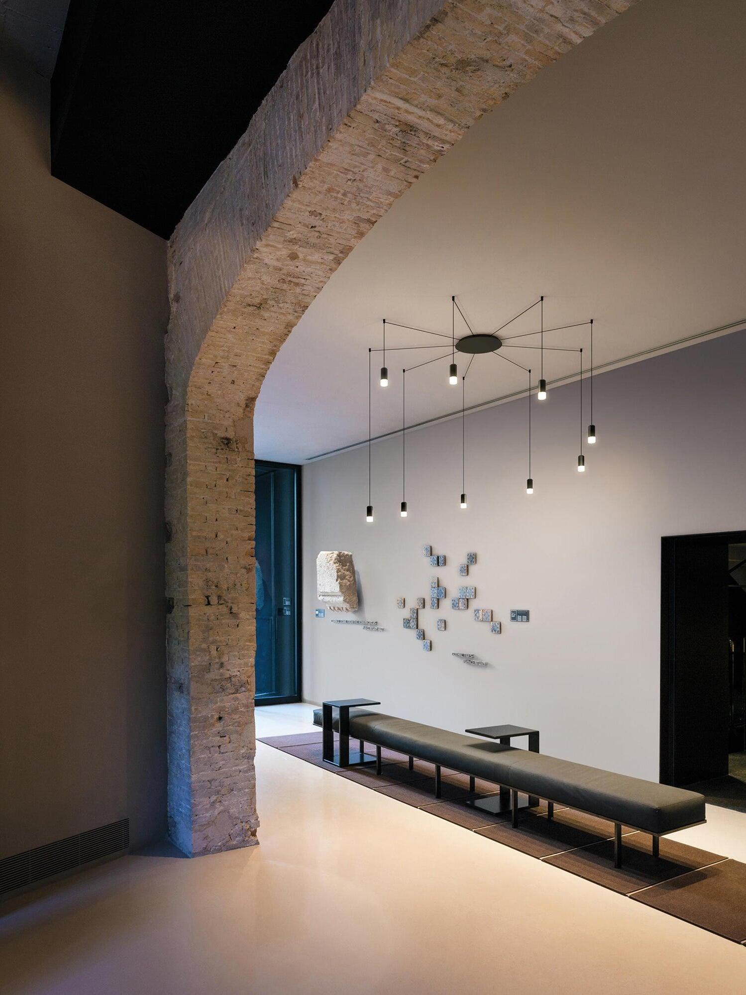 Cable pendants above a long bench and table beside a large stone arch and window