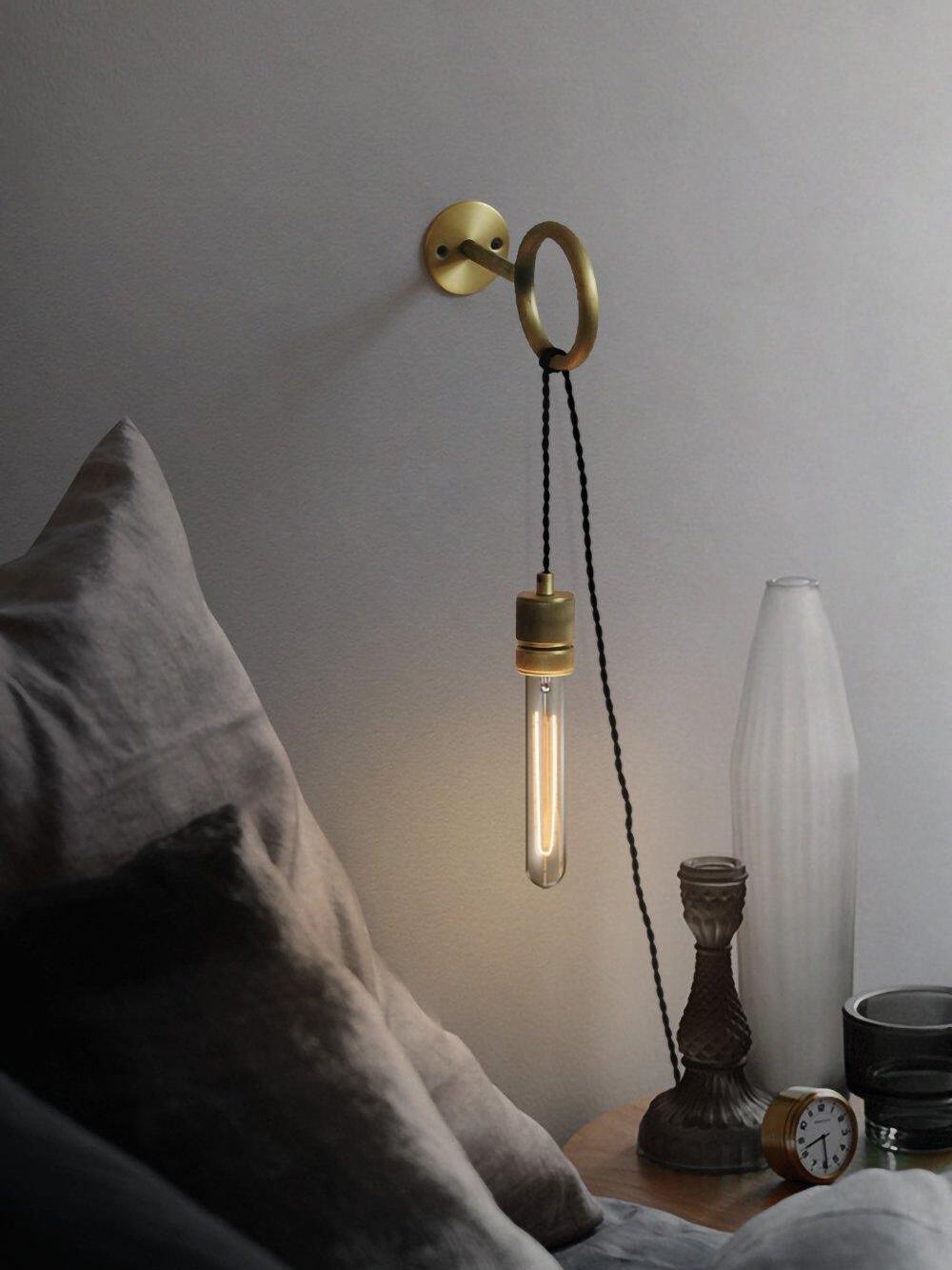 Hanging tubular bulb from loop bracket beside bed