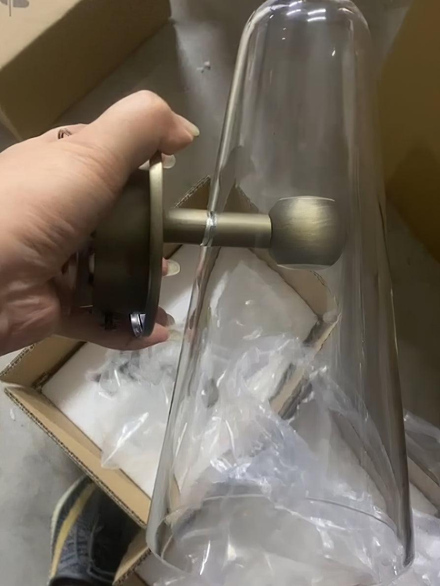 Hand holding a clear glass fixture with metal stem and round backplate