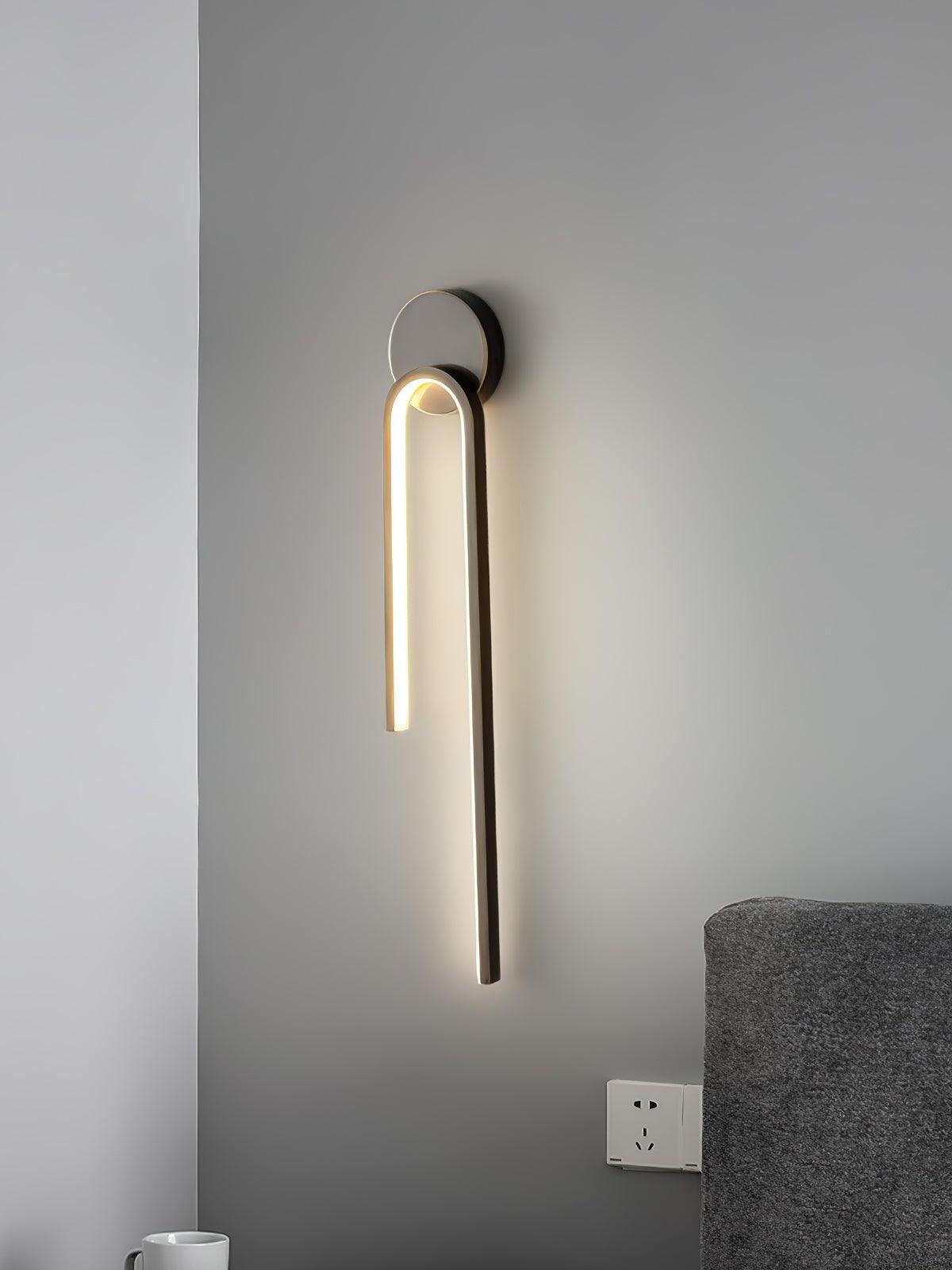 Dark arch wall light with a long right arm above a gray bedhead beside a pale corner wall
