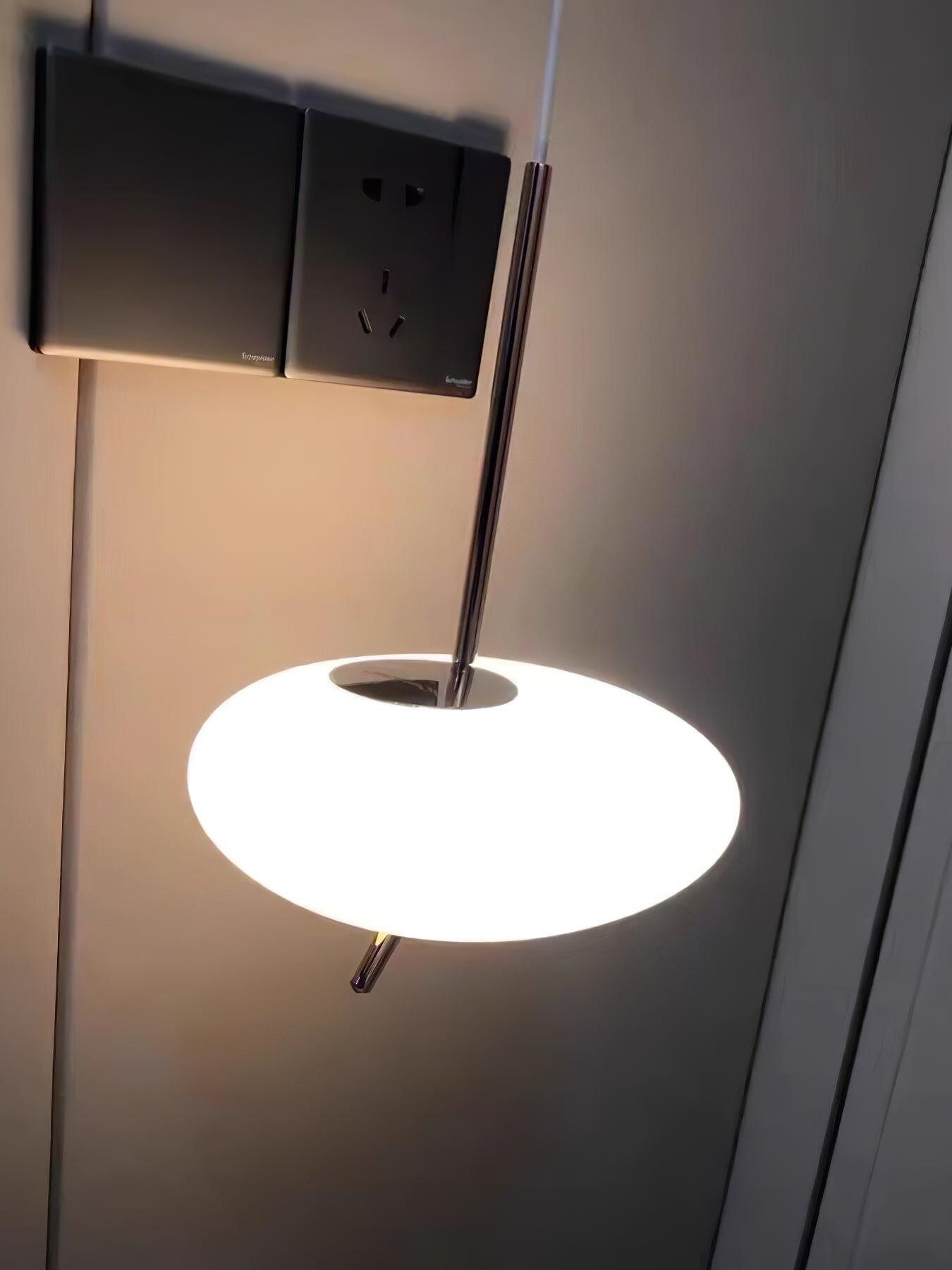 Low-angle close-up of a glowing white pendant and central stem near a dark ceiling panel