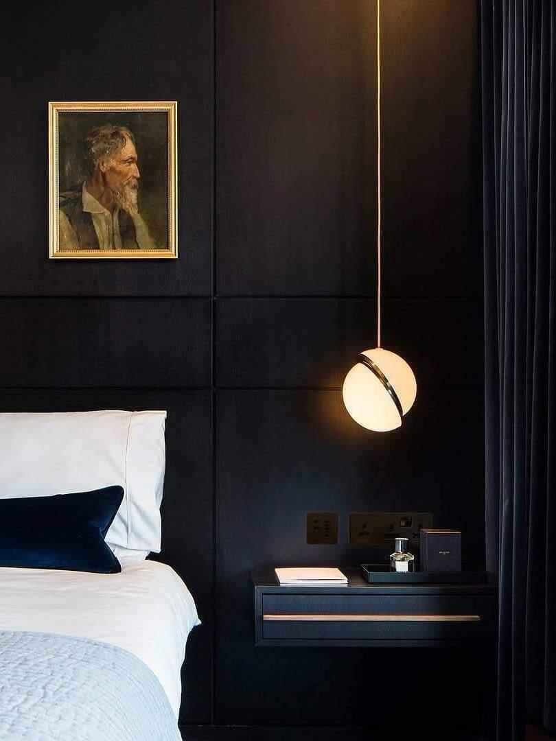 Single lit Crescent globe pendant beside a bed, dark wall panels and a portrait
