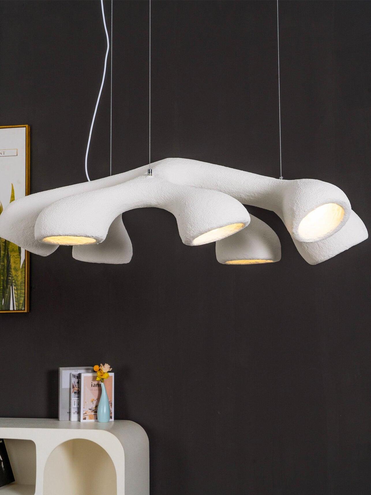 Glowing white branching pendant against a dark wall above an arched console with books and a small vase