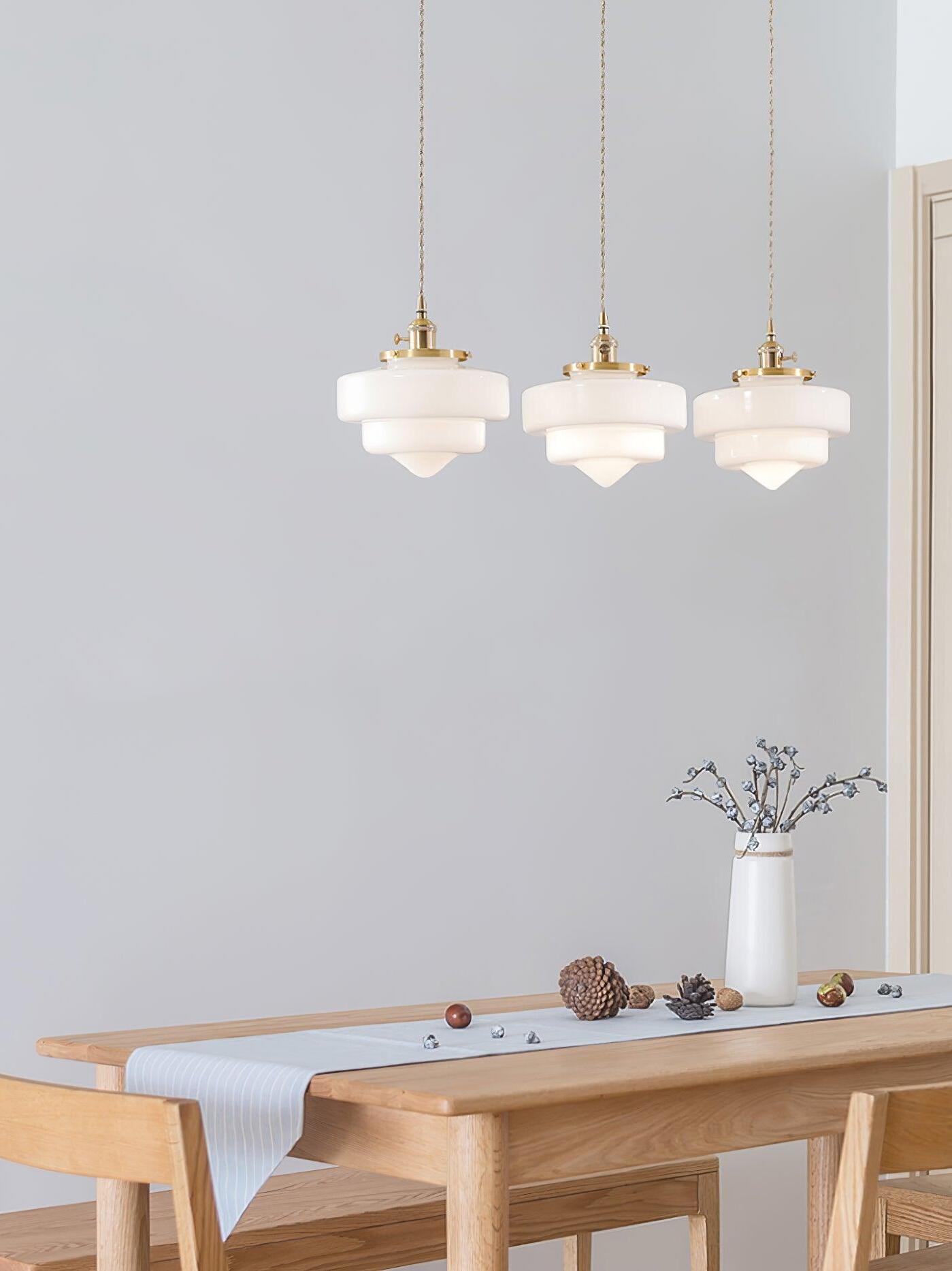 Three lit Atlas Model A shades above a wooden dining table with blue-gray runner, branch vase and chairs