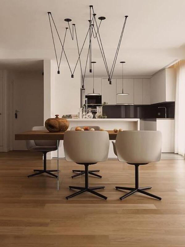 Black geometric lights over a wooden dining table and swivel chairs, with separate pendants in the kitchen behind