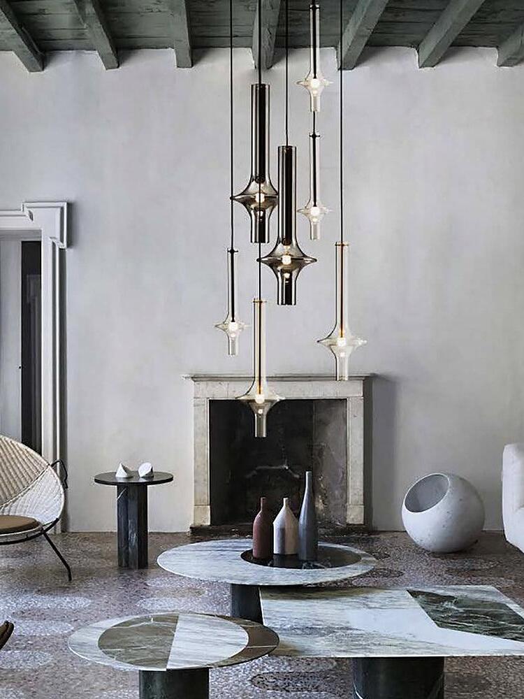 Six clear and smoky pendants at varied heights above stone coffee tables near a fireplace beneath exposed ceiling beams