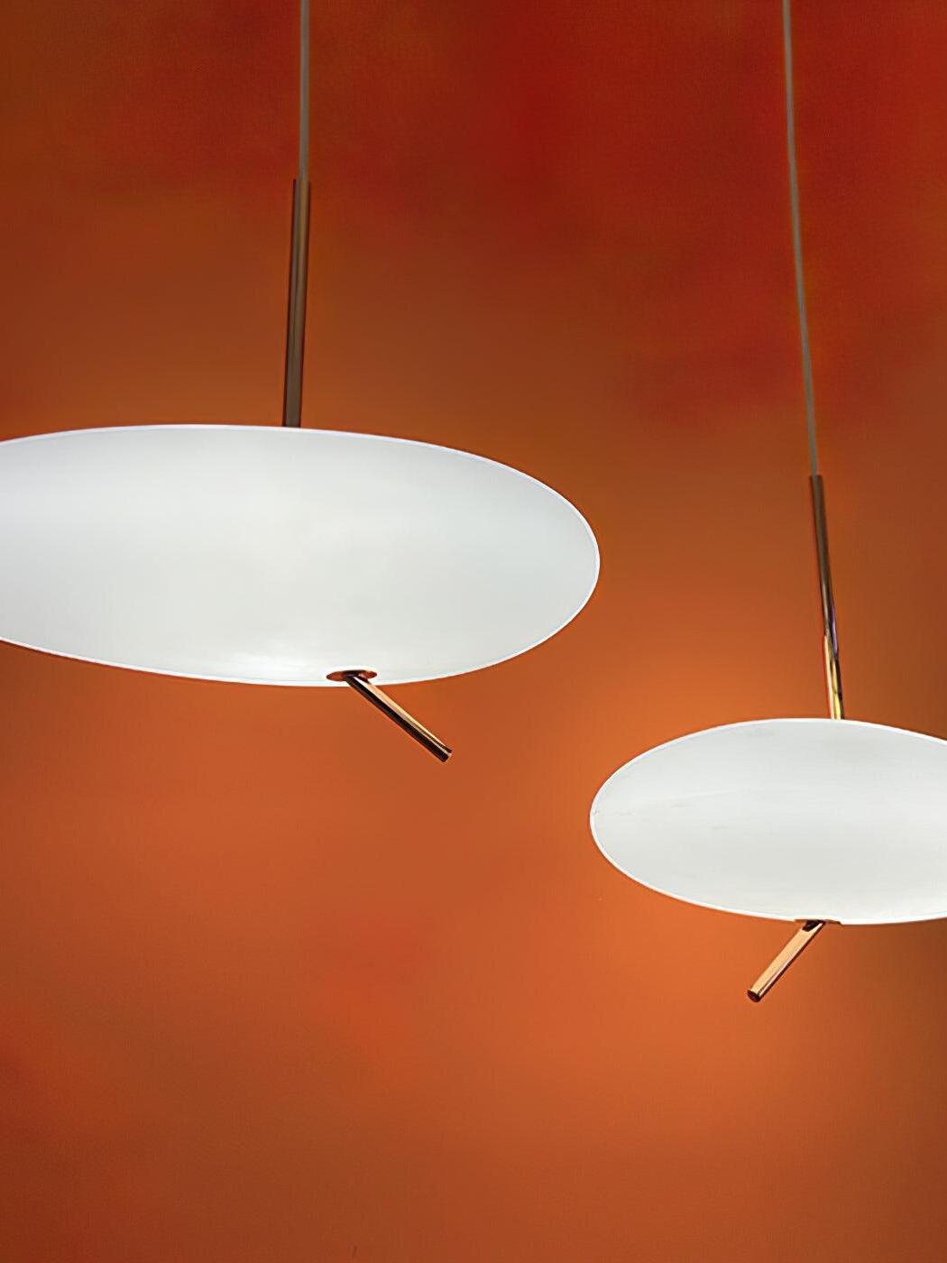 Two white flattened pendant shades with rose-gold stems against an orange wall