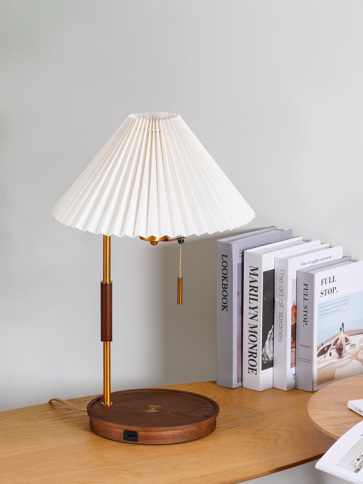 Unlit white pleated table lamp with a dark wood base and stem collar beside a row of books