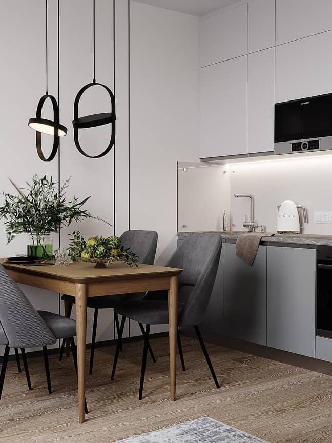 Two vertical black oval-frame pendants with tilted discs over a wooden dining table in a white kitchen