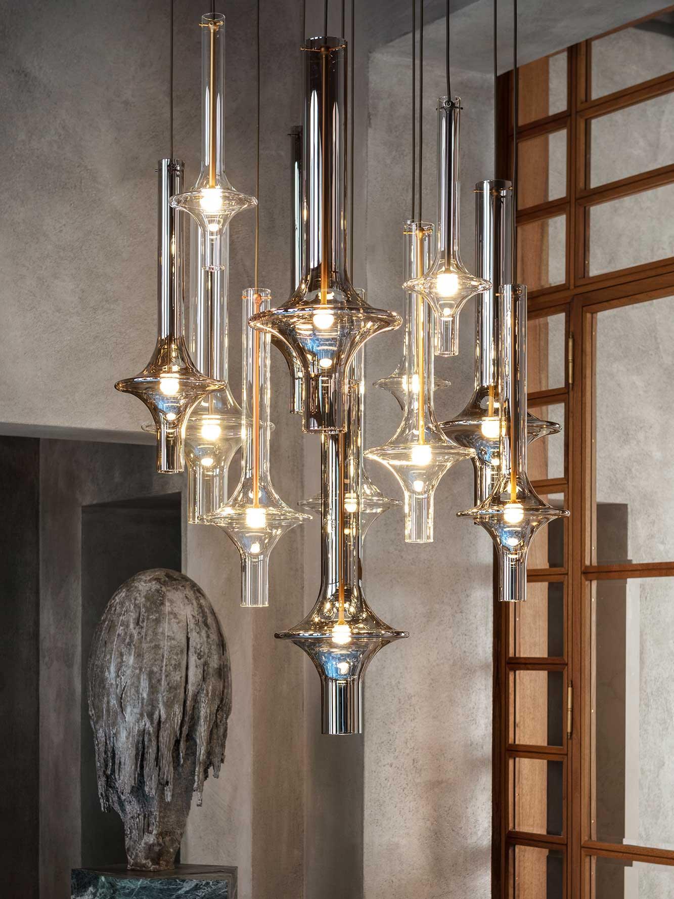 Closer view of mixed clear and smoky glass pendants by a wooden window grid and tall stone sculpture