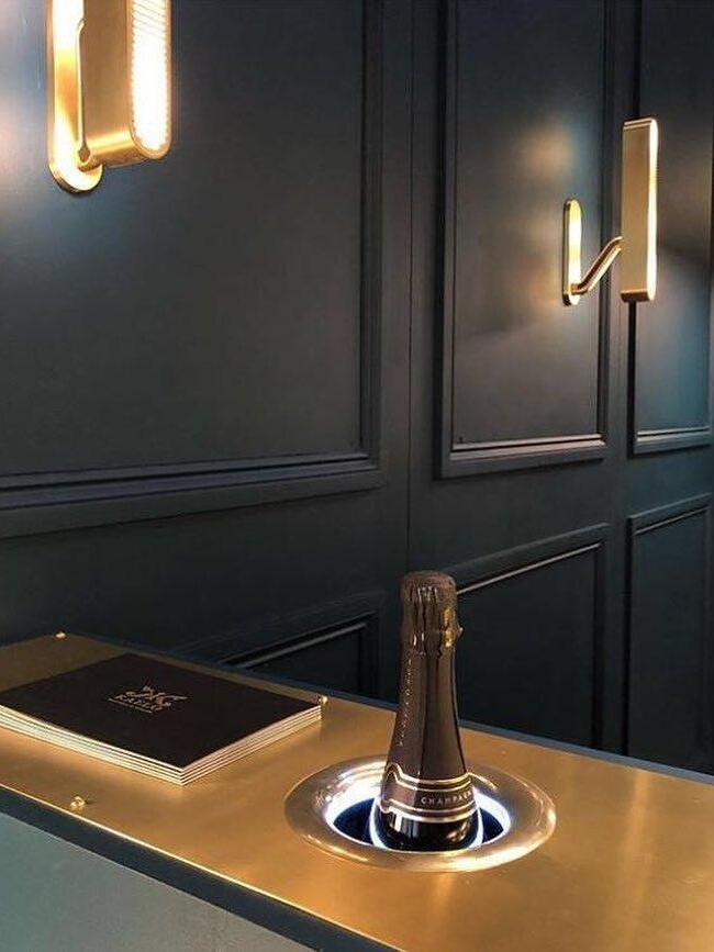 Oblique view of lit wall bars on Dark Blue panels beside a counter with a bottle and menu, near light partly cropped