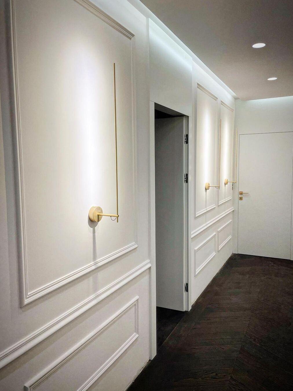 Gold rod sconce along a panelled corridor