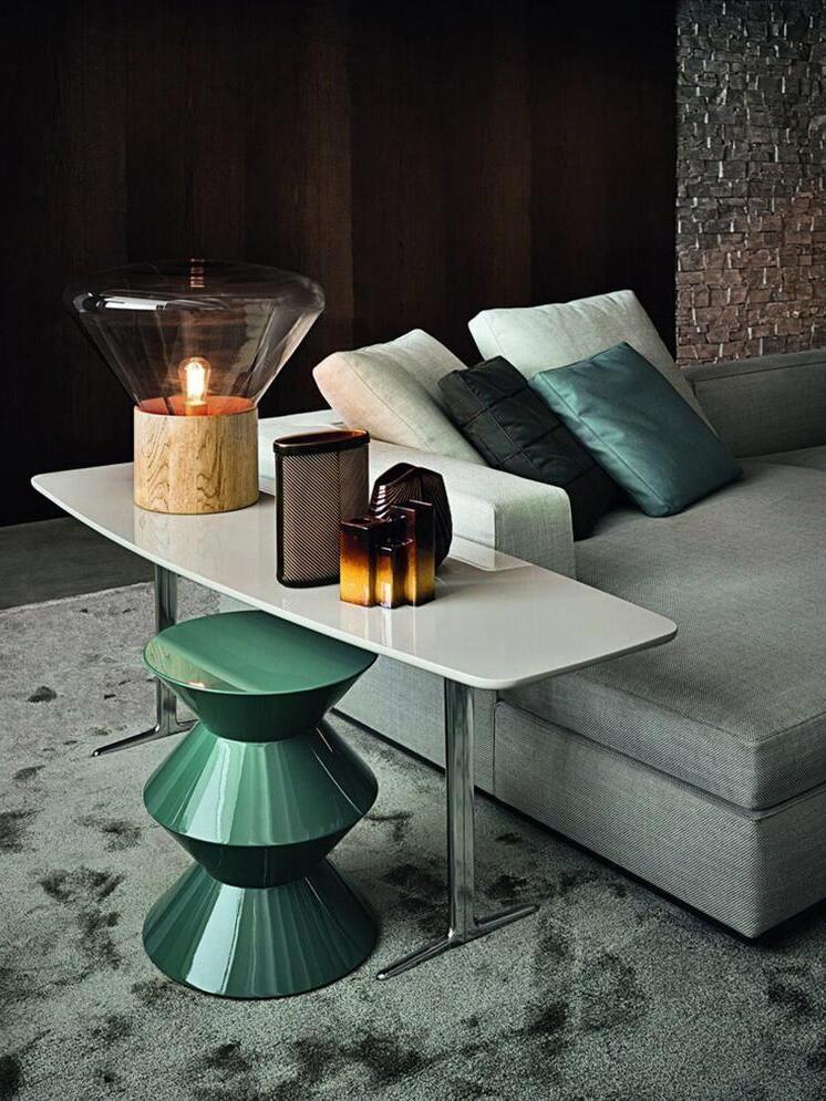 Lit smoky glass lamp on side table beside sofa, green stools and bottles