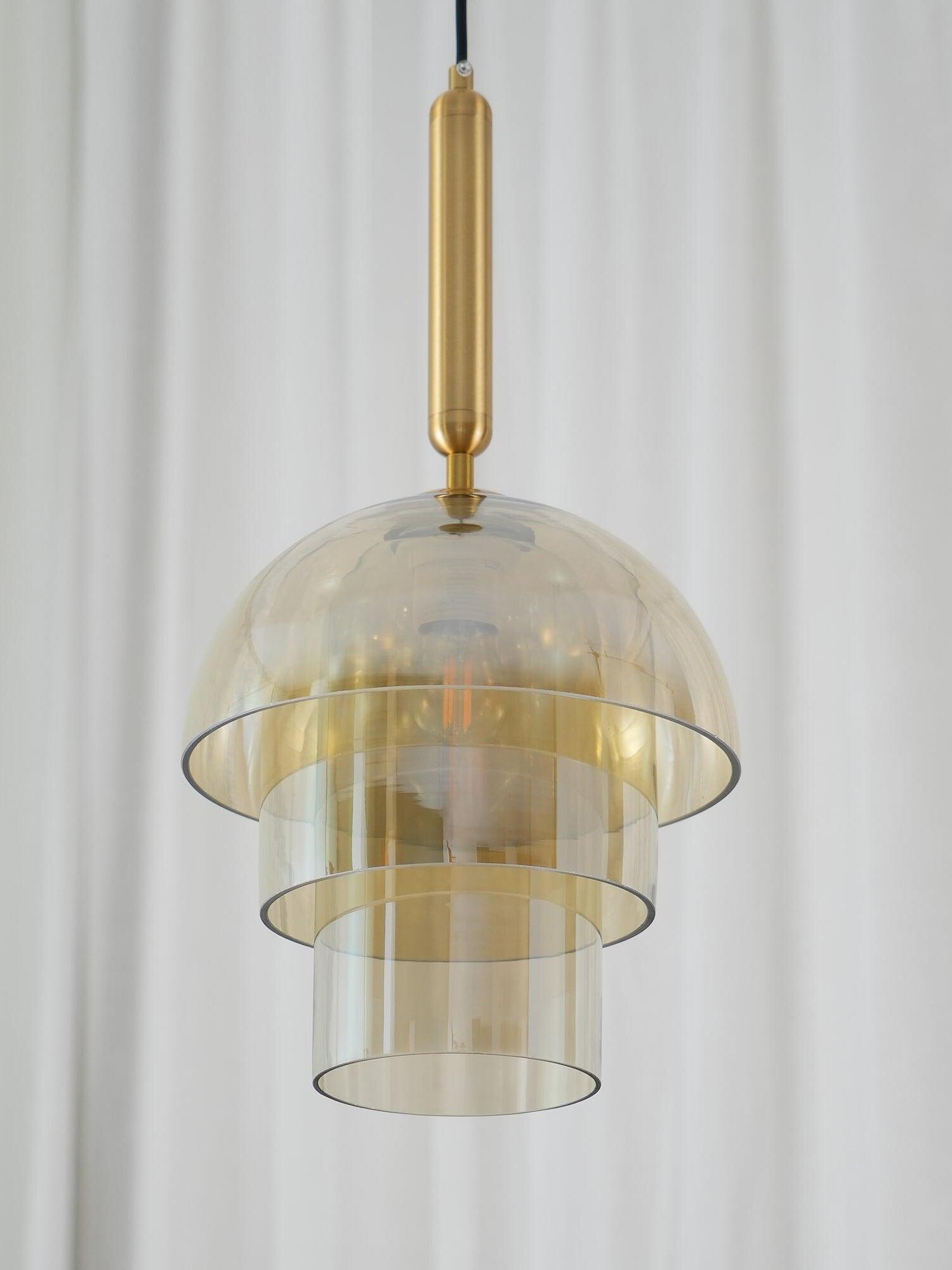 Three-tier glass pendant detail against white curtains, with reflective amber dome, narrower cylinders and gold-tone fitting
