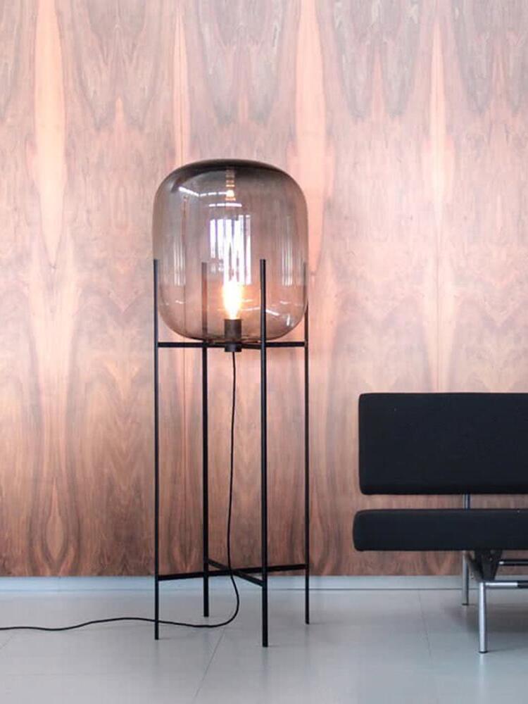 Illuminated smoke-toned glass floor lamp against a pink textured wall.