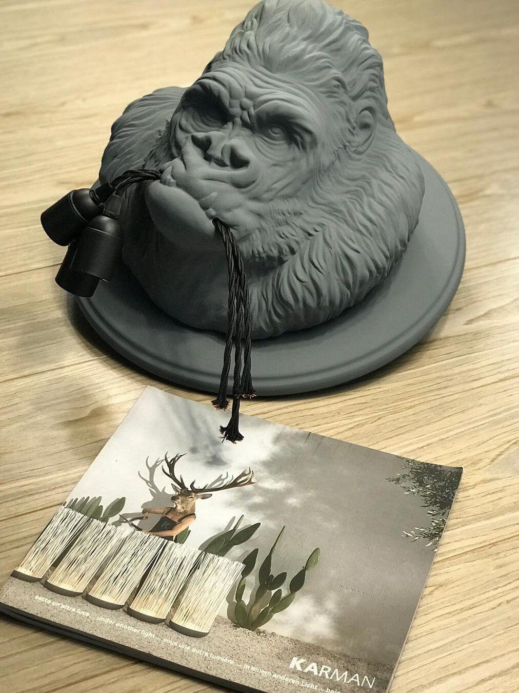 Grey sculpted gorilla head laid on wood tabletop beside lighting catalog