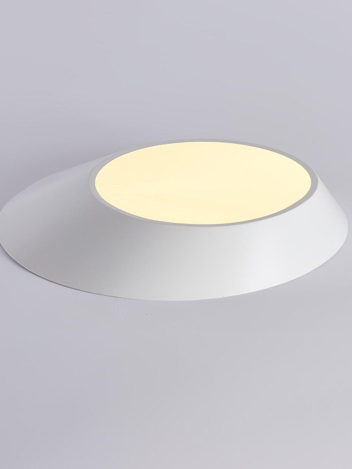 White angled ceiling light resting upside down, showing its glowing round diffuser and sloping body