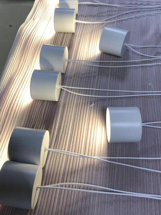 White cylindrical light heads with bright circular faces and white wires resting on striped fabric