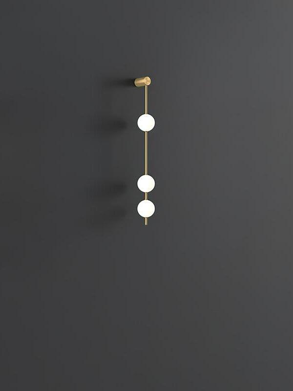 Three-globe gold-colour wall lamp with an upper fitting and wall shadows against dark grey