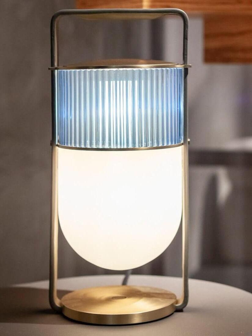 Illuminated Xi lamp with pale blue-grey ribbed upper glass and glowing white lower shade against wood
