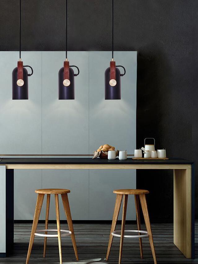 Three black cylindrical pendants in a row over a counter with cups, teapot, wooden stools and pale blue cabinets
