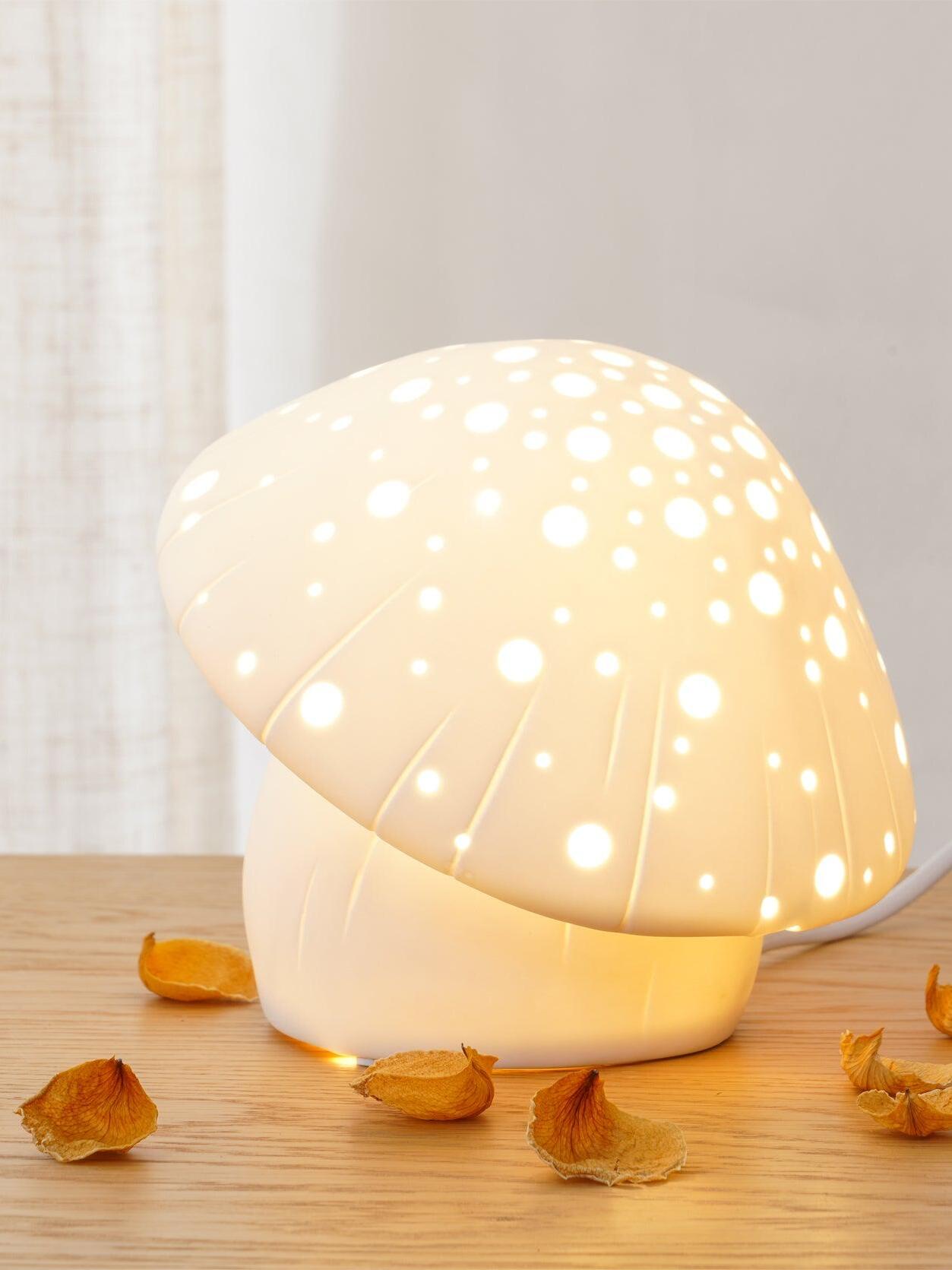 Illuminated Fungo lamp on a wooden surface beside scattered petals and a sheer curtain