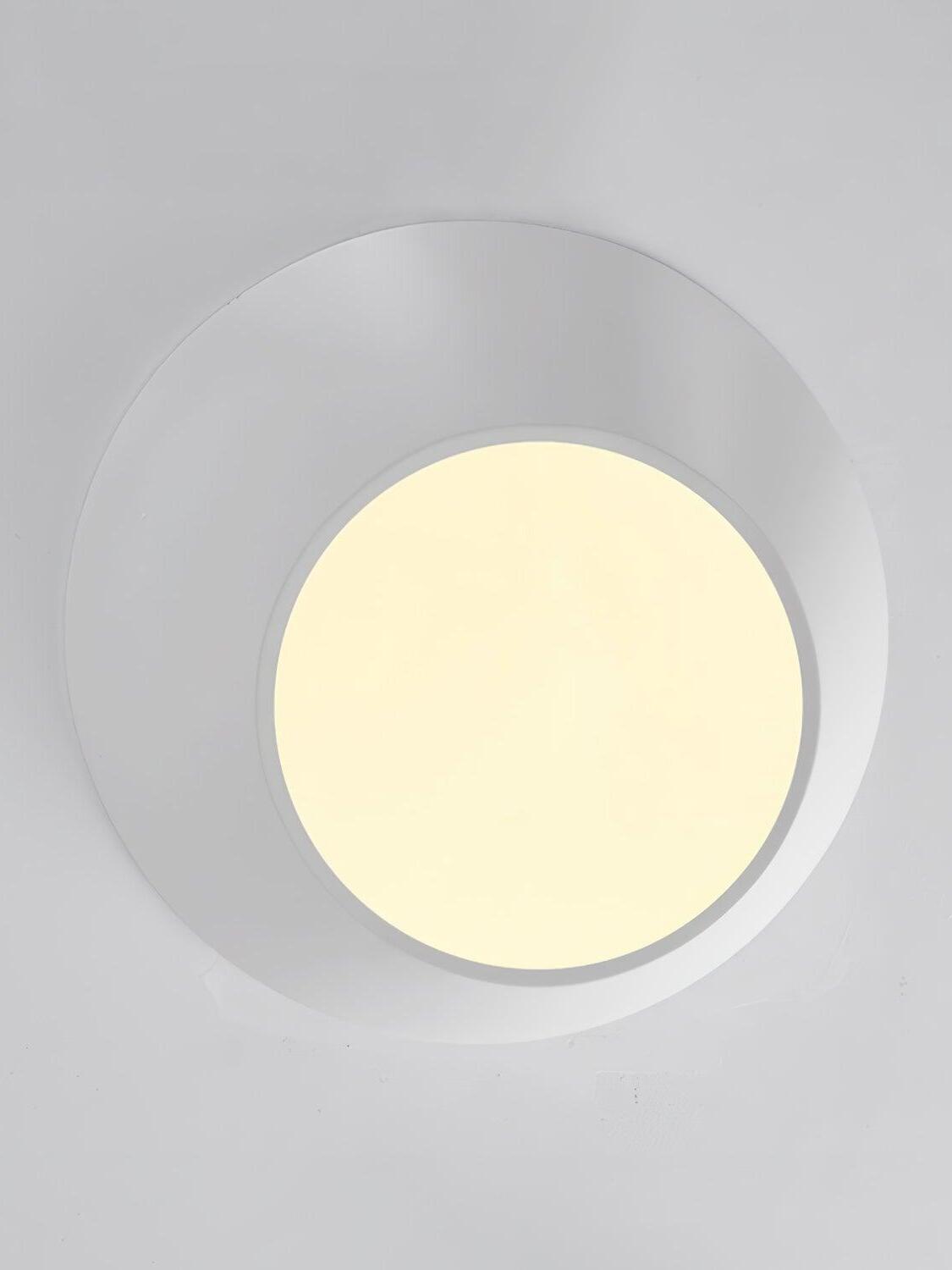 Underside of a white angled ceiling light with a warm-looking circular diffuser and unequal rim