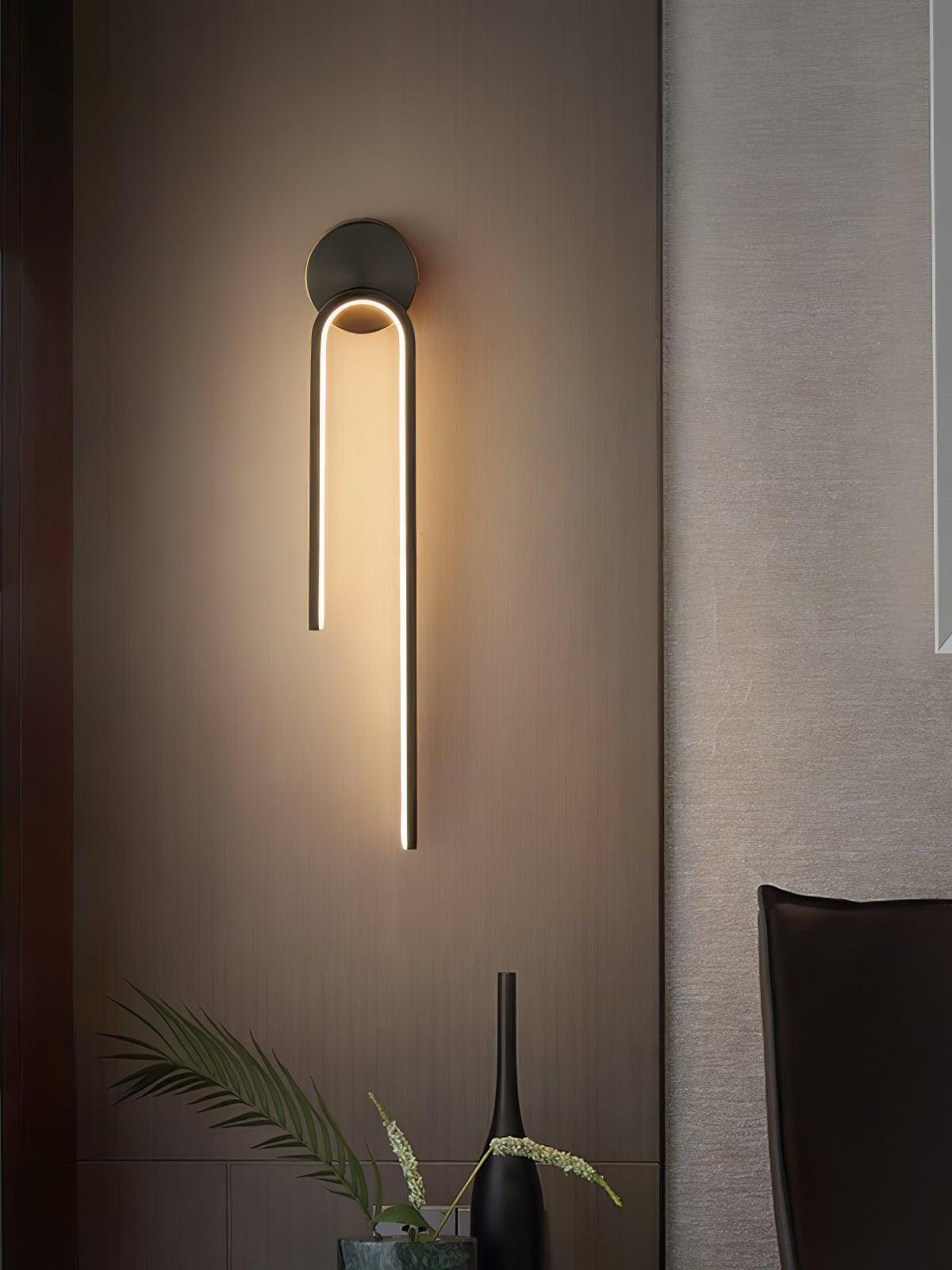 Dark arch wall light with a long right arm on a wood wall above a plant and tall vase