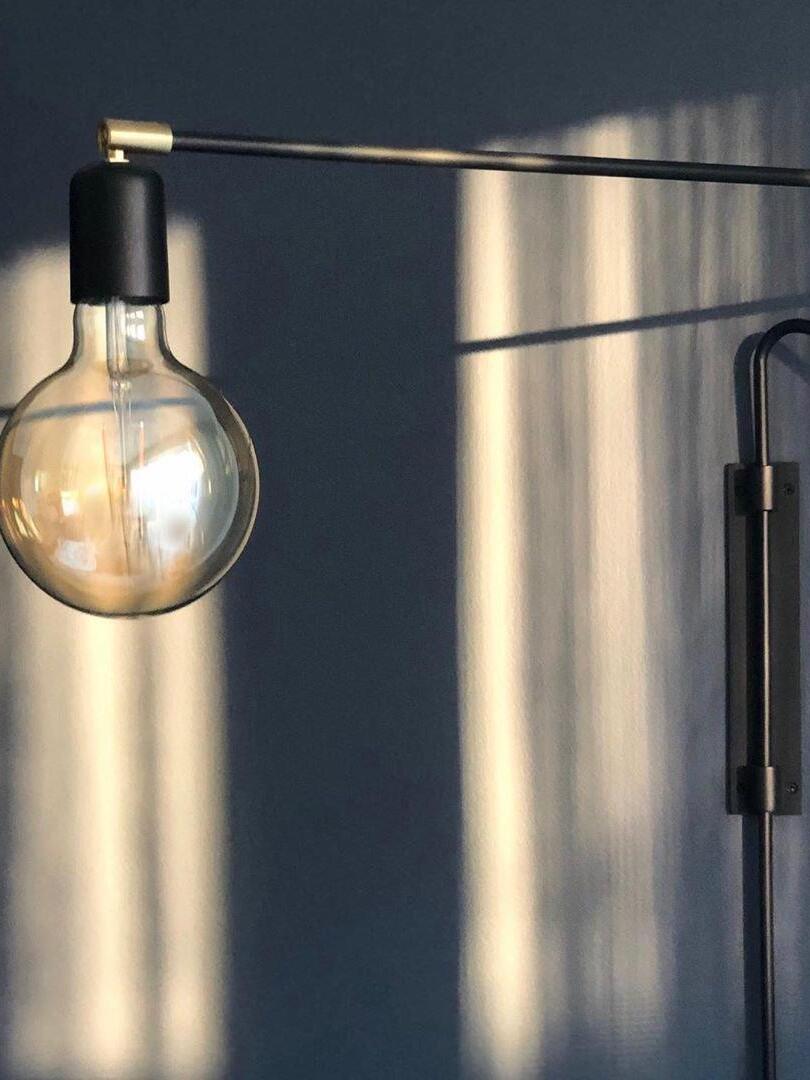 Close-up of black bulb holder, brass-tone end joint and glowing globe bulb against a dark wall