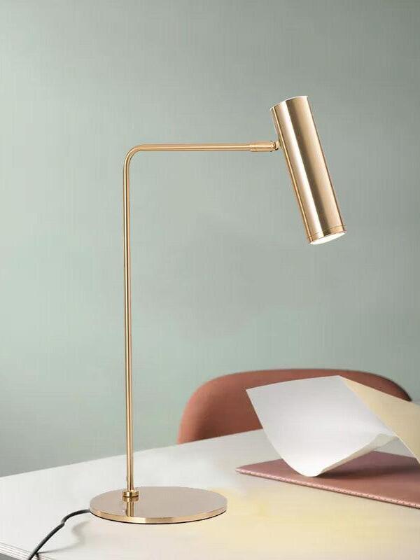 Gold-tone angled-head lamp on desk beside chair and papers against green wall