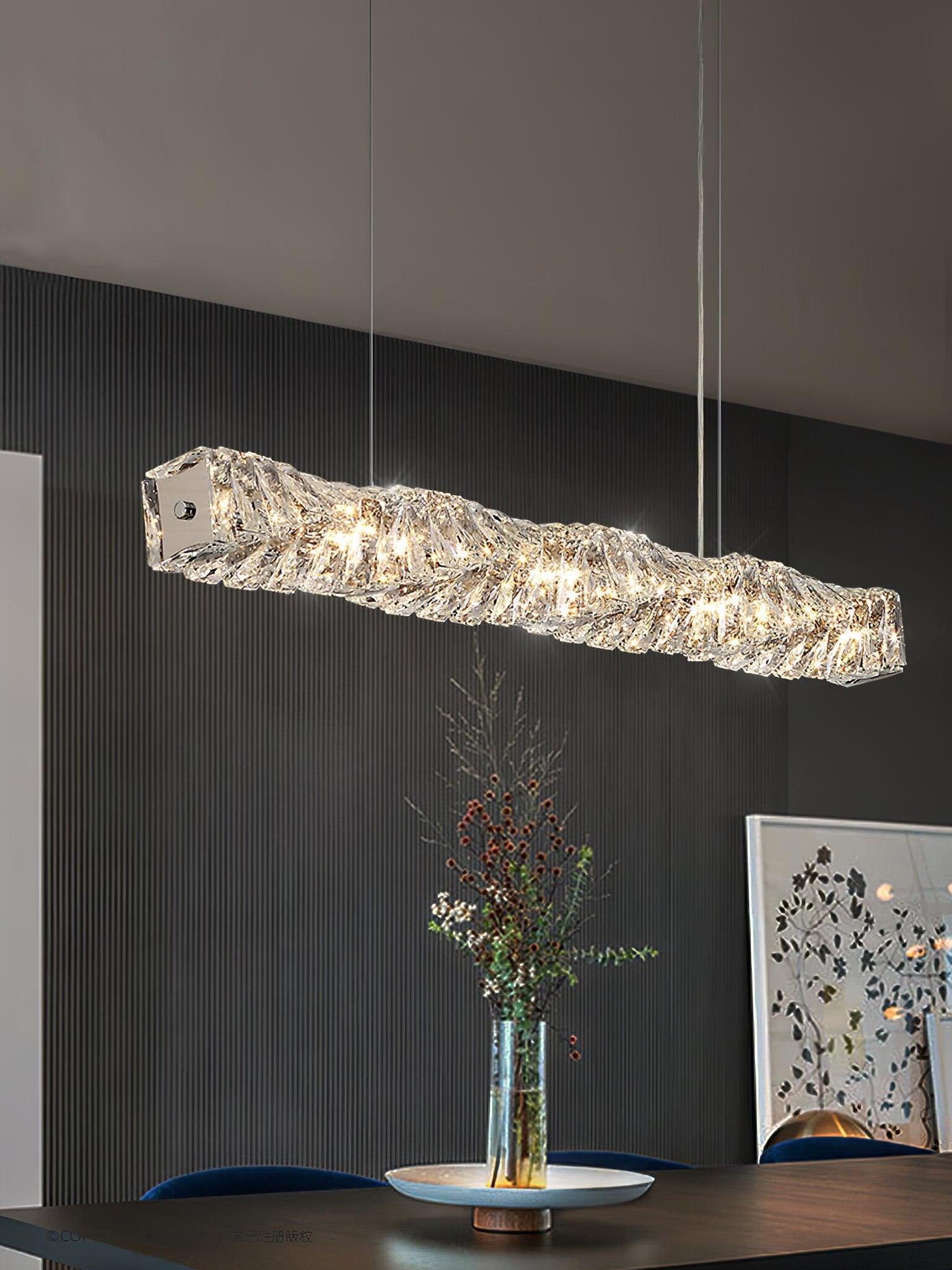 Diagonal crystal pendant above a dark table with a vase and framed artwork