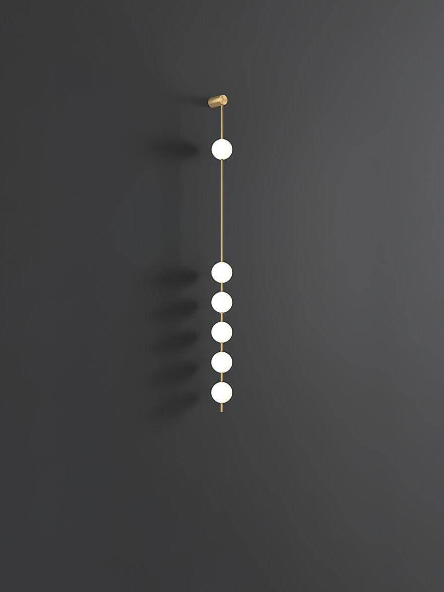 Six white globes on a vertical gold-colour rod against dark grey with wall shadows