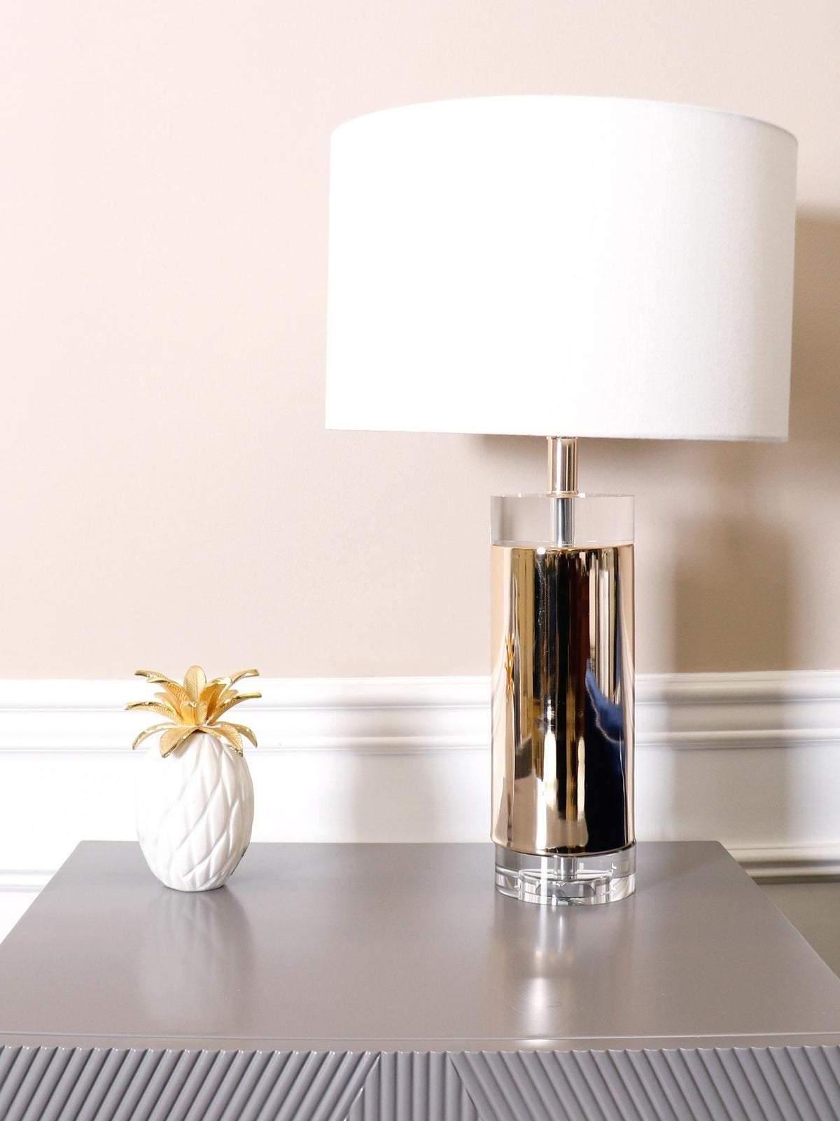 White-shade gold-tone table lamp on grey surface beside small white vase