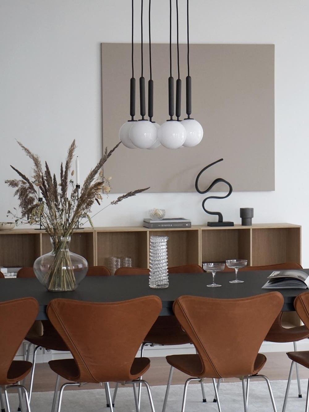 White globe pendants on black stems above a dining table with a sideboard behind