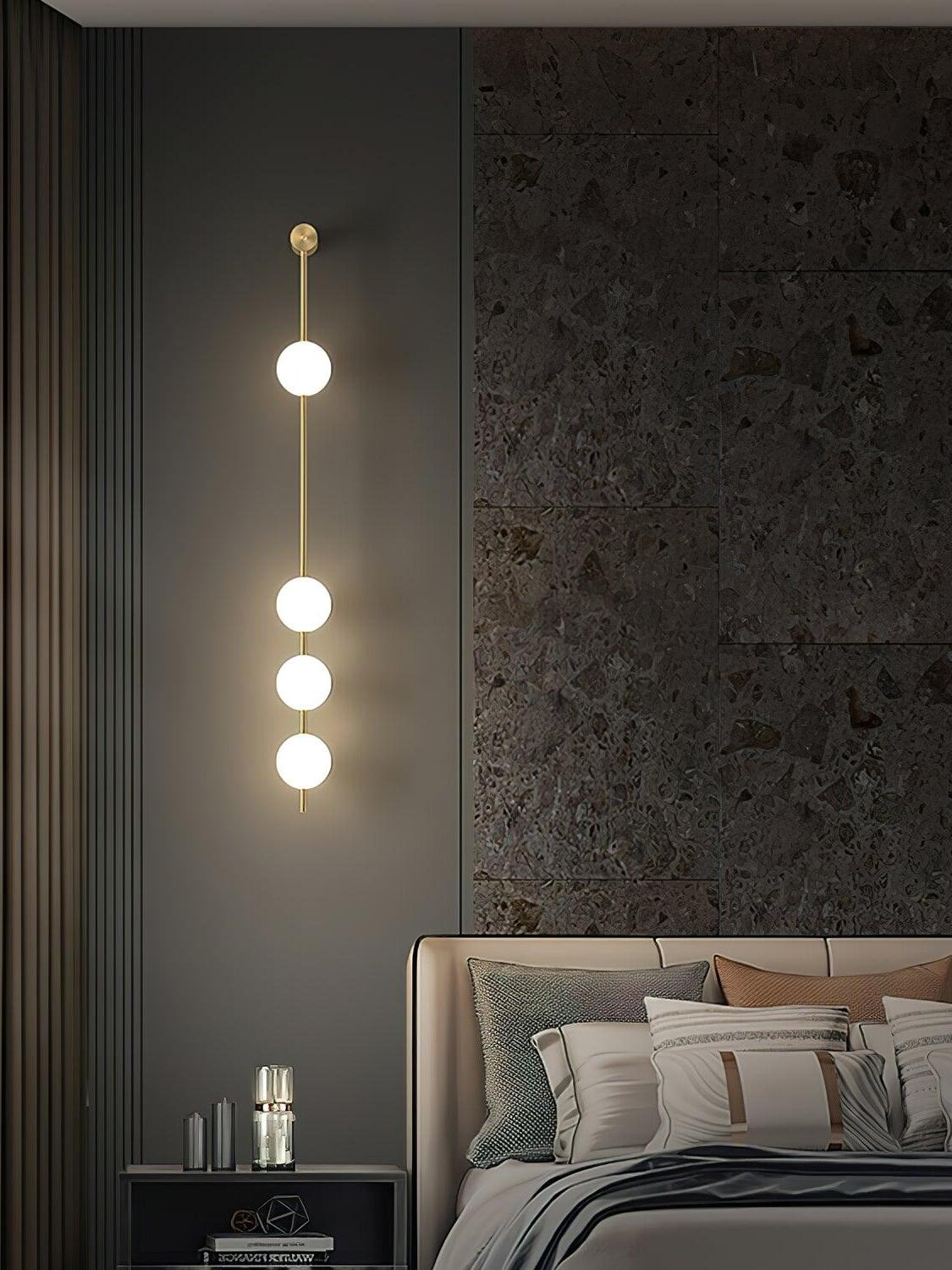 Four-globe wall light on a grey wall beside an upholstered bed and dark fluted panel